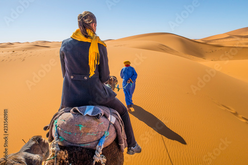 Berber nomad and a young girl riding camel in Sahara desert, Morocco