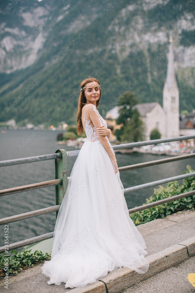 A beautiful bride walks near a lake on a mountains background in a fairy Austrian town, Hallstatt. A beautiful bride walks near a lake on a mountains background in a fairy Austrian town, Hallstatt.