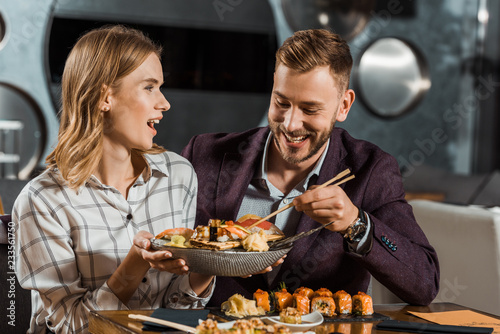 Beautfiful surprised woman holding plate with delicious seafood while couple having dinner in restaurant