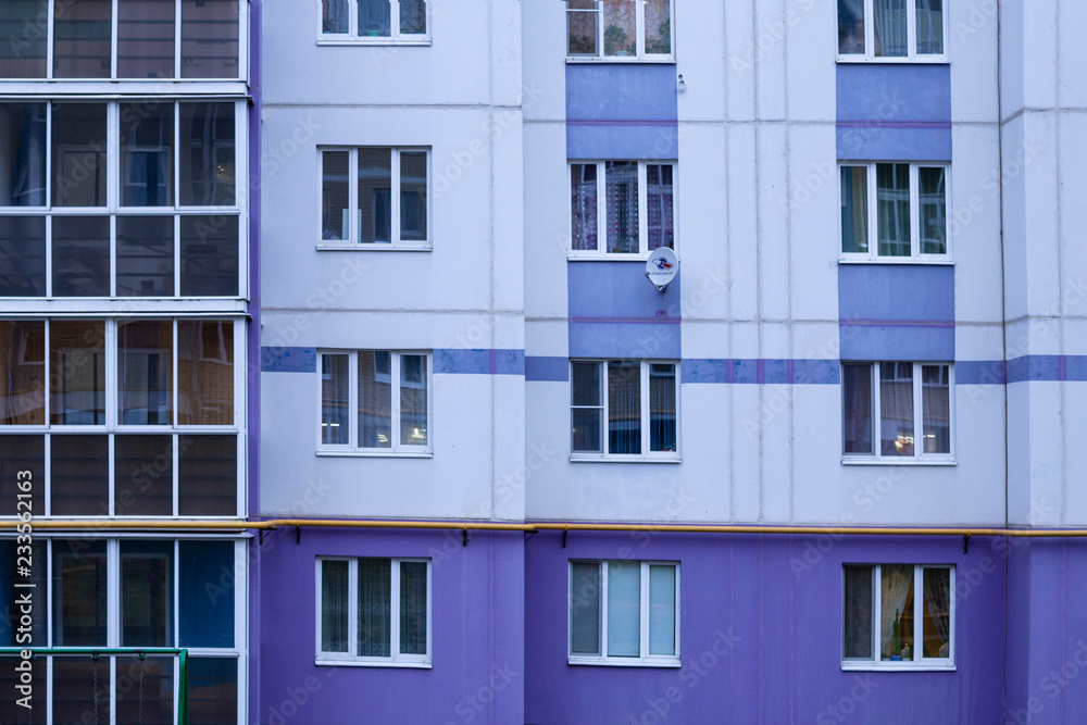 the wall of a multi-storey house with balconies in gray, blue and purple tones