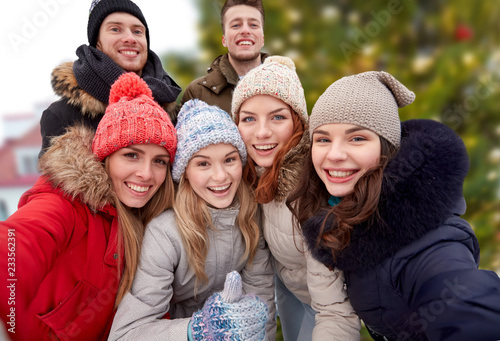 holidays, friendship and people concept - happy friends showing thumbs up over christmas tree background