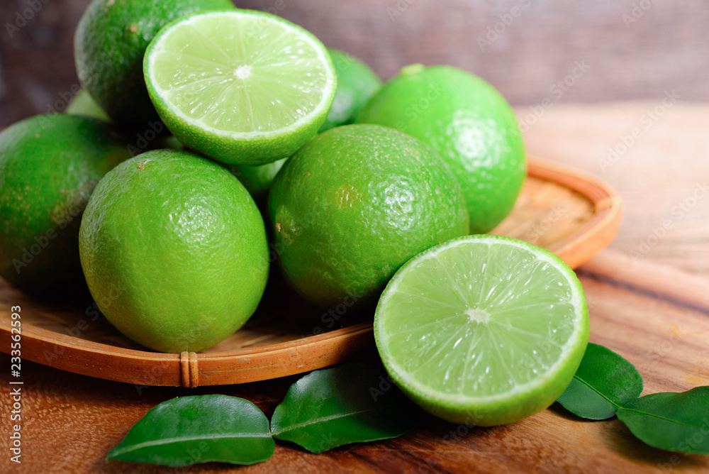 whole and half cut fresh lime in bamboo basket and on wooden background whole and half cut fresh lime in bamboo basket and on wooden background