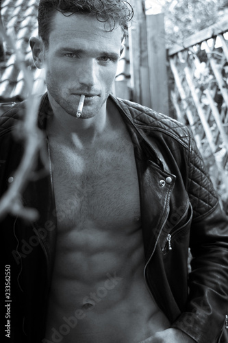 Handsome blonde man with open leather jacket revealing sixpack abs smoking cigarette and looking at camera