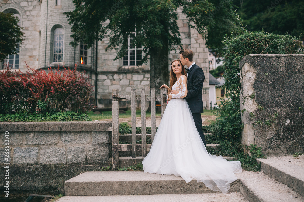 Fototapeta premium A beautiful wedding couple posing on a background old cathedral in a fairy Austrian town, Hallstatt.