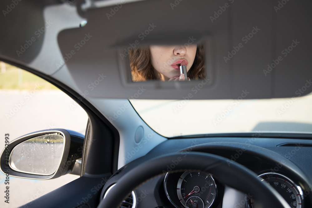 girl putting makeup her lips on the car with the mirror