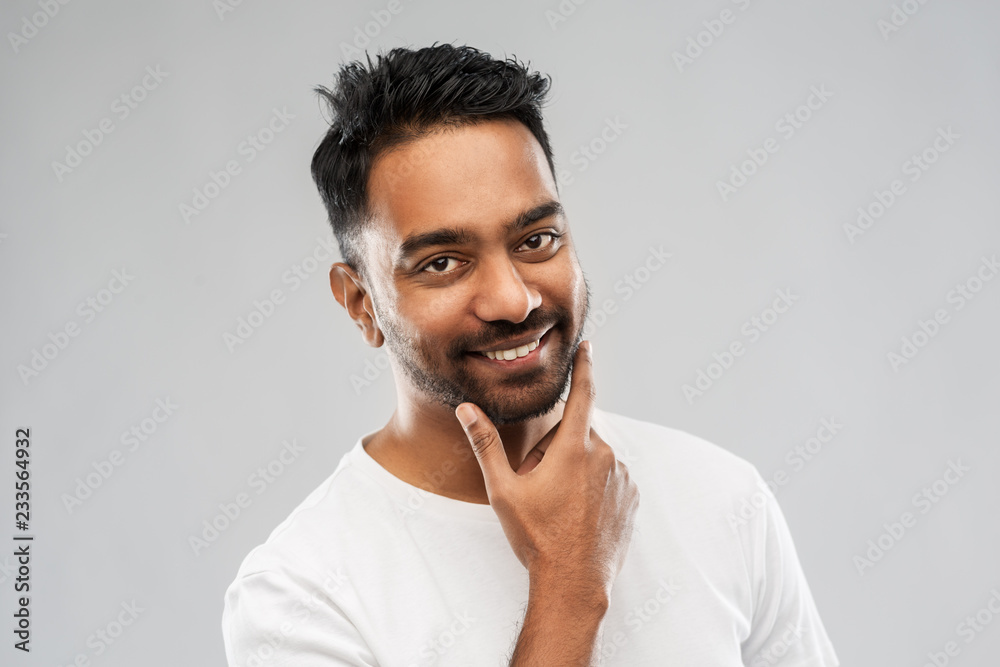 grooming and people concept - smiling indian man touching his beard over gray background grooming and people concept - smiling indian man touching his beard over gray background