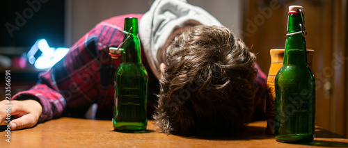 young drunk man with glass and bottle of alcohol lying on the table  f photo