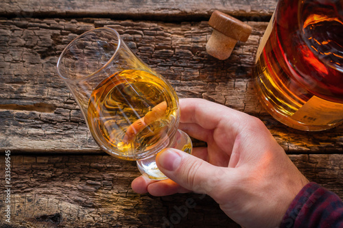 hand holds whiskey in a glass for tasting on a wooden background