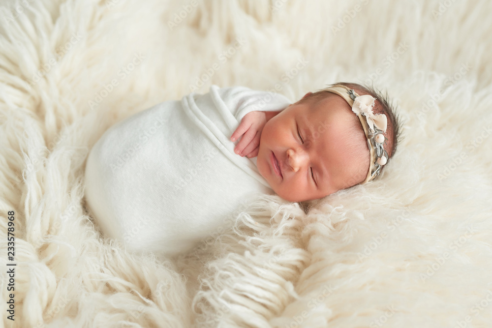 Cute newborn baby girl lies swaddled in a white blanket. Baby goods