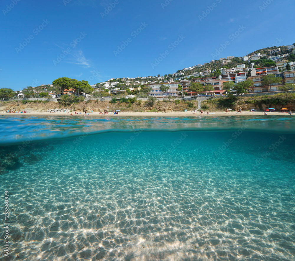 Beach coastline with buildings in Roses town and sand underwater, split view half above and below water surface, Spain, Costa Brava, Mediterranean sea, Catalonia