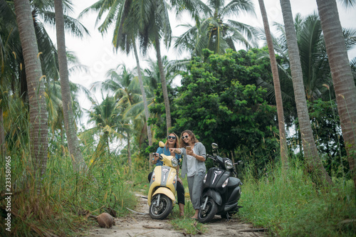 A pair of beautiful women travel by scooter through the jungle in Southeast Asia. Phone navigation