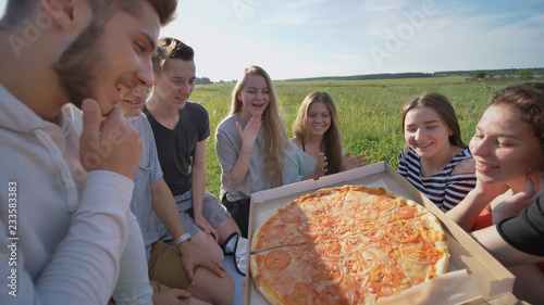 Friends of schoolchildren eat pizza outdoors during the sunset in the evening.