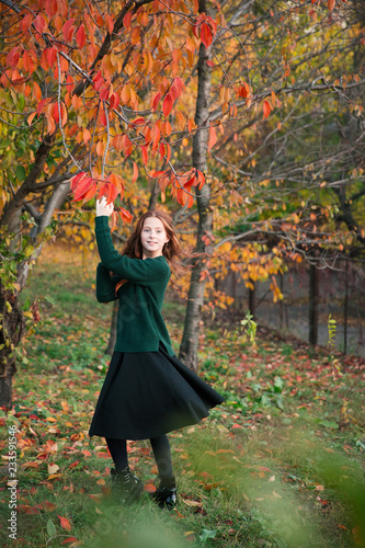 Red-hair girl dancing and playing in the autumn garden full of colorful leaves.