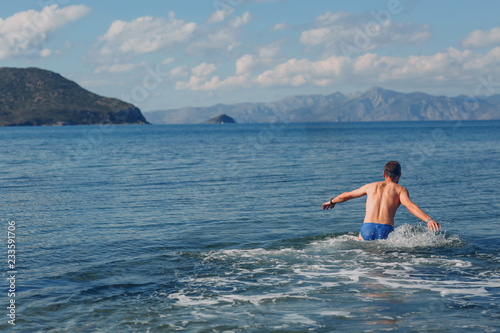 A young man swims in the sea against the backdrop of mountains