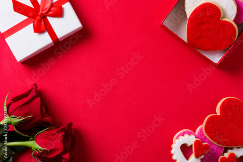 Heart-shaped cookies for Valentine's Day and roses in gift box on red background. Top view. Copyspace