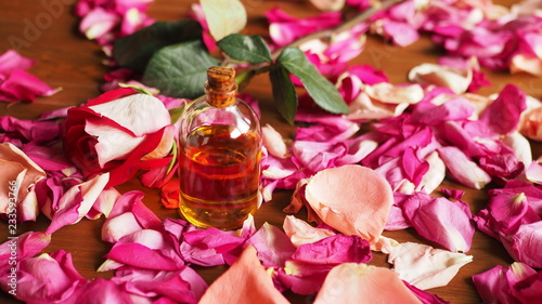 Aroma oil glass bottle among roses petals on the table, natural raw material, selected focus