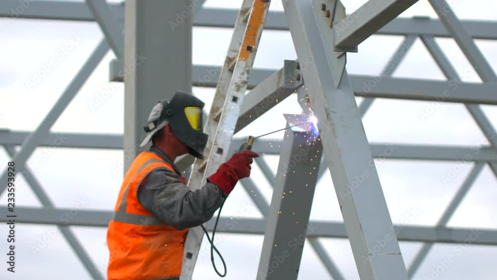 Industrial worker welding of metal structures, welder man male worker soldering steel beam structure on new building on construction site. welder working. Sparks fly as one welder welds steel.
