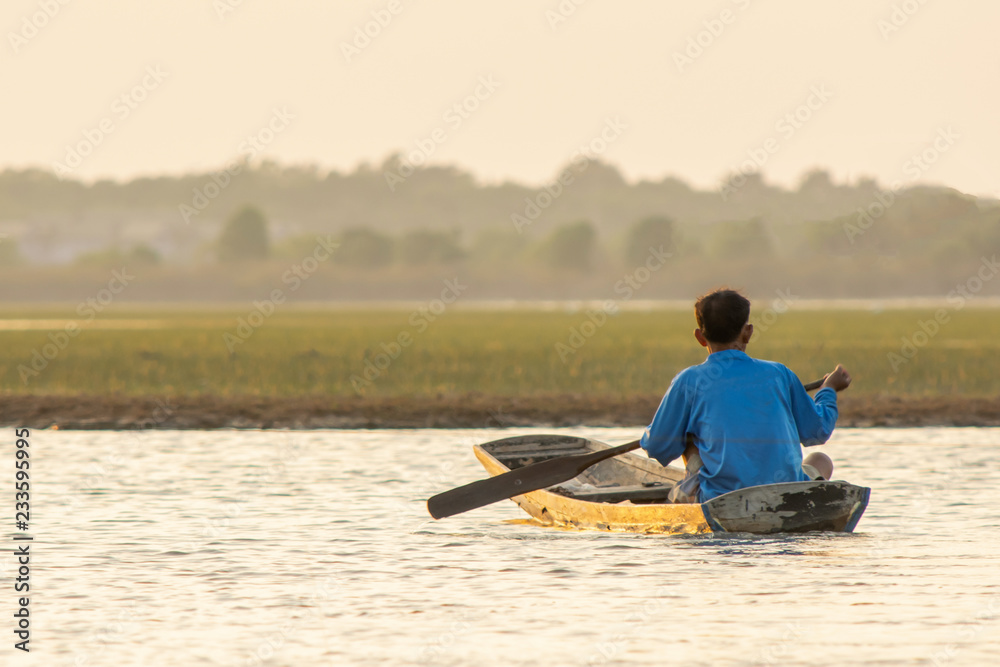 NAKHON PHANOM, THAILAND - OCT 11, 2018 :Old man paddle wooden boat in the lake for fishing NAKHON PHANOM, THAILAND - OCT 11, 2018 :Old man paddle wooden boat in the lake for fishing