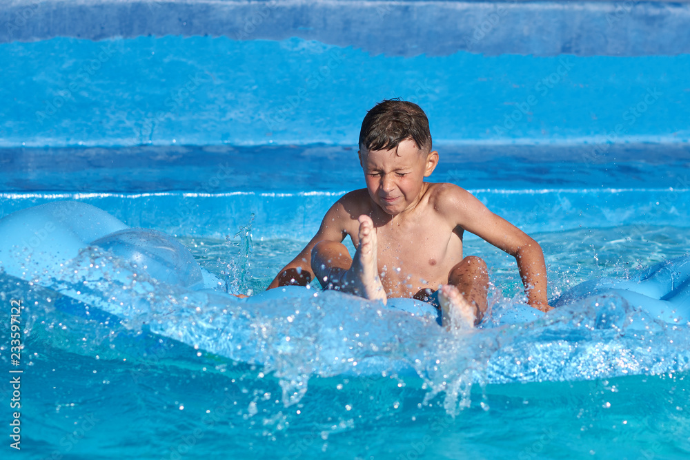 Boy having fun making jump from inflatable mattress into swimming pool at resort.