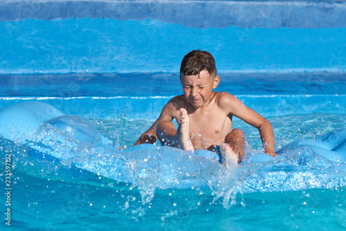 Boy having fun making jump from inflatable mattress into swimming pool at resort.