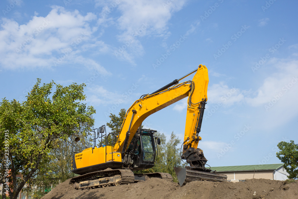 yellow excavator on the soil pile against blue sky yellow excavator on the soil pile against blue sky