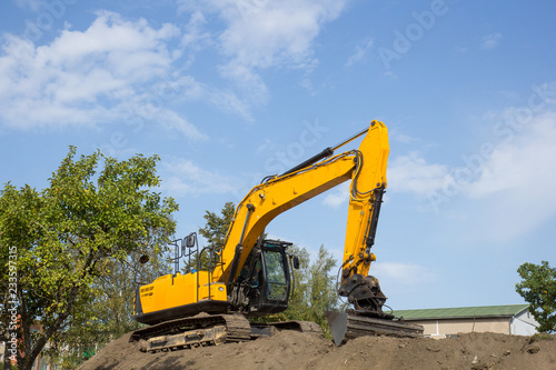 yellow excavator on the soil pile against blue sky