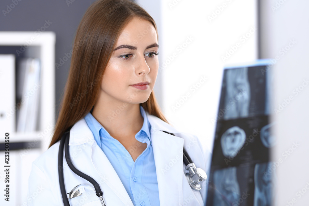 Doctor woman examining x-ray picture while standing near window in hospital. Surgeon or orthopedist at work. Medicine and healthcare concept Doctor woman examining x-ray picture while standing near window in hospital. Surgeon or orthopedist at work. Medicine and healthcare concept