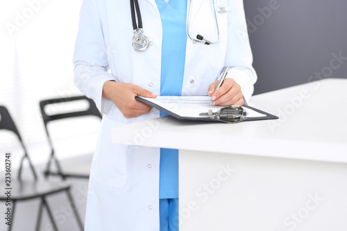Unknown doctor woman at work, hands close-up. Female physician filling up medical form while standing near reception desk at clinic or emergency hospital. Medicine and healthcare concept