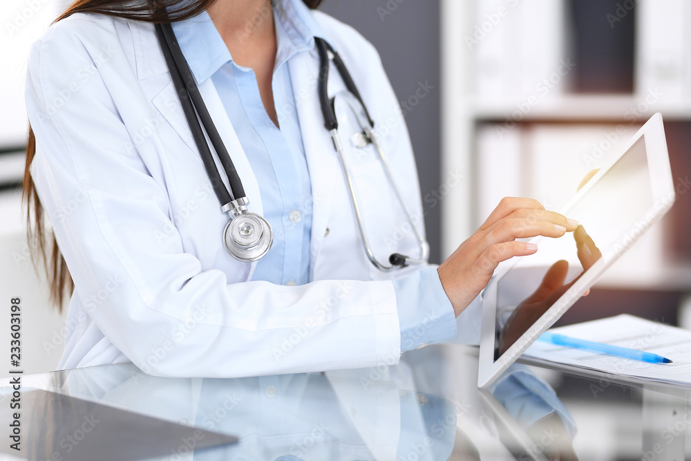 Close-up of female physician hands using digital tablet while sitting at glass desk at hospital office. Medicine and healthcare concept Close-up of female physician hands using digital tablet while sitting at glass desk at hospital office. Medicine and healthcare concept