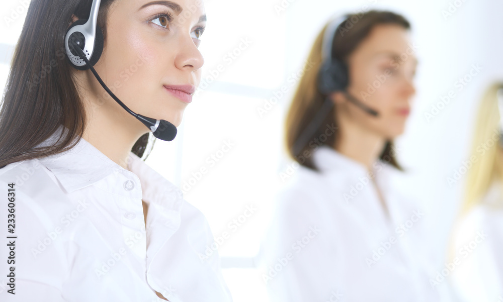 Group of call center operators at work. Focus on beautiful business woman in headset