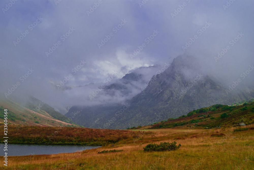 misty mountain valley with lush autumn vegetation and small lake, sheltered by low clouds