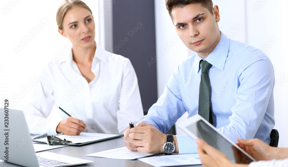 Obraz premium Group of business people or lawyers discussing terms of transaction in office. Colleagues working all together. Focus on young businessman. Meeting and teamwork concept