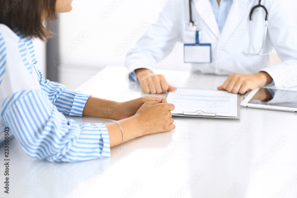 Doctor and patient talking and discussing health treatment while sitting at the desk, close-up. Medicine and health care concept Doctor and patient talking and discussing health treatment while sitting at the desk, close-up. Medicine and health care concept
