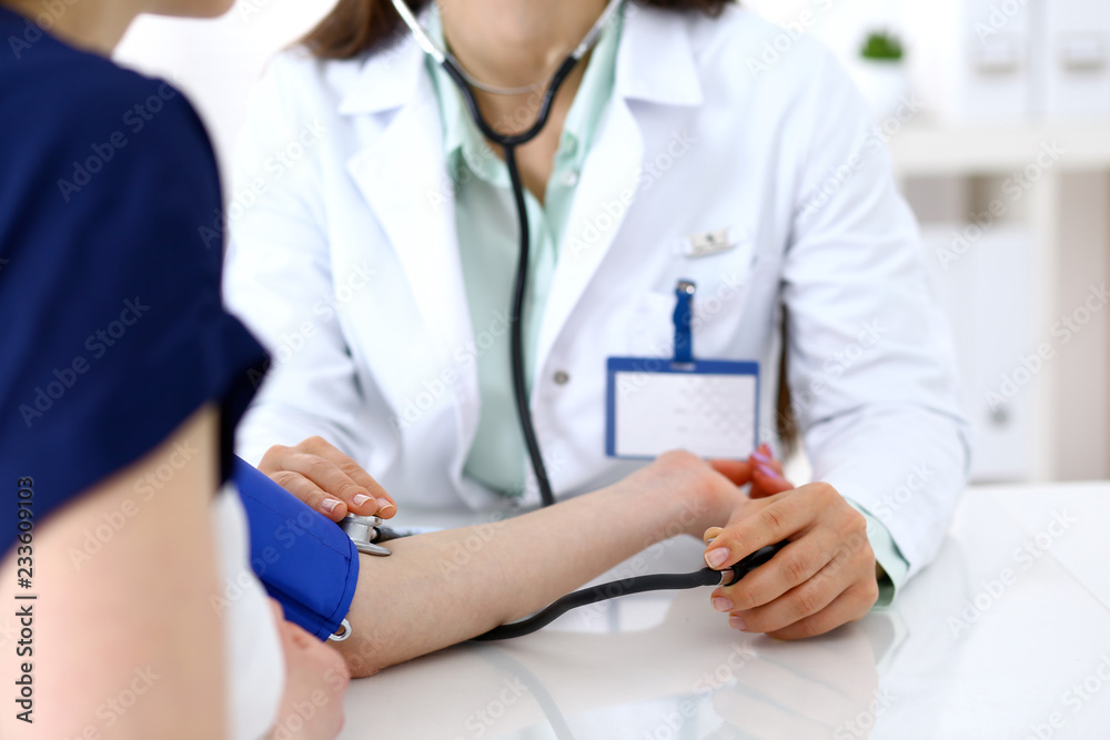 Doctor woman checking blood pressure of female patient, close-up. Cardiology in medicine and health care concept Doctor woman checking blood pressure of female patient, close-up. Cardiology in medicine and health care concept
