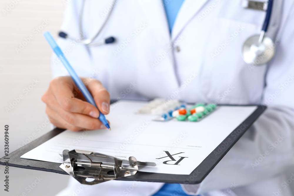 Woman doctor at work at hospital. Young female physician write prescription or filling up medical form while sitting in hospital office, close-up Woman doctor at work at hospital. Young female physician write prescription or filling up medical form while sitting in hospital office, close-up