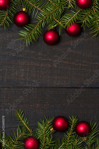 Dark rustic wooden table background with Christmas decoration -  fir and red ornament frame. Top view with free space for copy text
