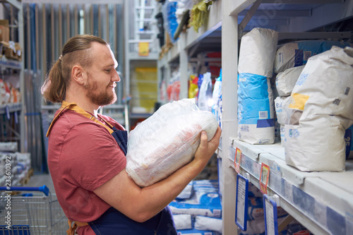 Young bearded salesman carries a pack of plaster in counstruction store photo