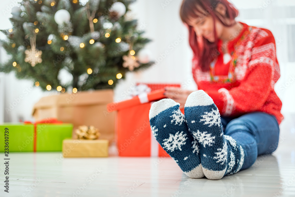 Feet in woolen socks by the christmas tree, woman looking at gift boxes Feet in woolen socks by the christmas tree, woman looking at gift boxes
