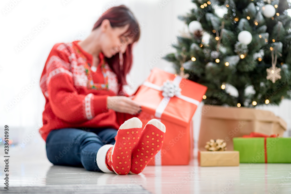 Feet in woolen socks by the christmas tree, woman looking at gift boxes