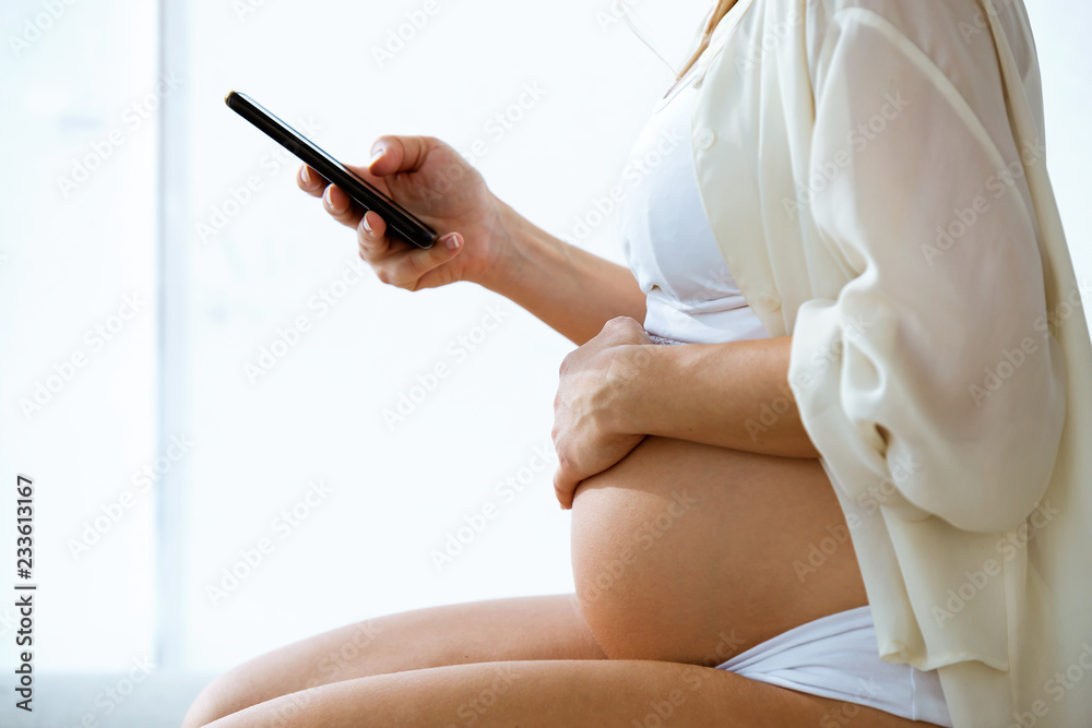 Pregnant woman texting with her smartphone sitting at home. Pregnant woman texting with her smartphone sitting at home.