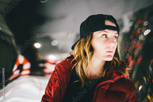 Trendy charming girl in red jacket wearing stylish cap with pensive face