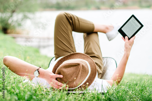 Girl with hat reading e book while lying on the grass