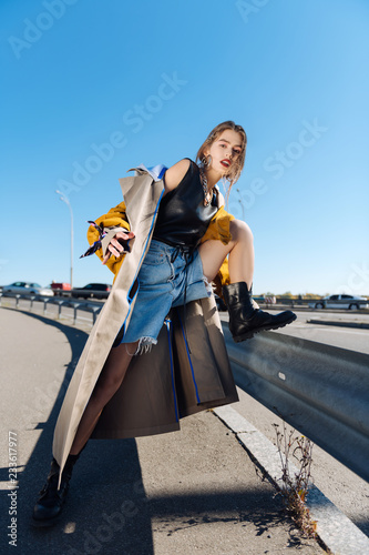Skinny trendy fashion model posing near the bridge wearing long coat
