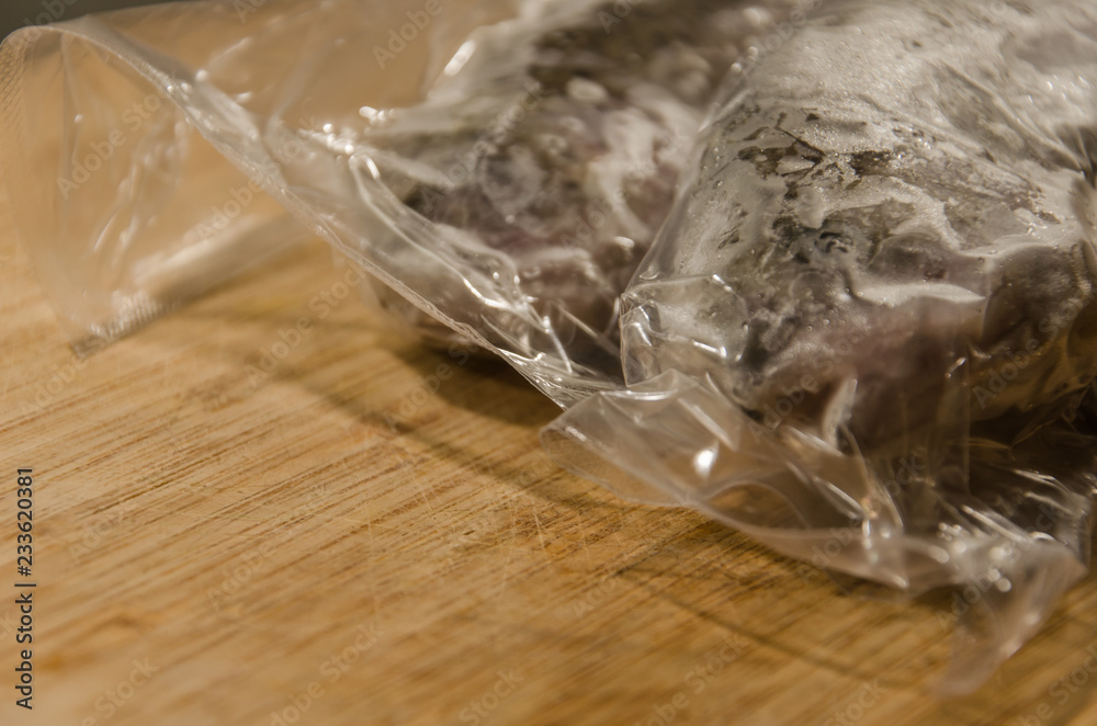 Sealed and frozen rainbow trout fish in plastic packing on wooden table in kitchen, ready for cooking Sealed and frozen rainbow trout fish in plastic packing on wooden table in kitchen, ready for cooking
