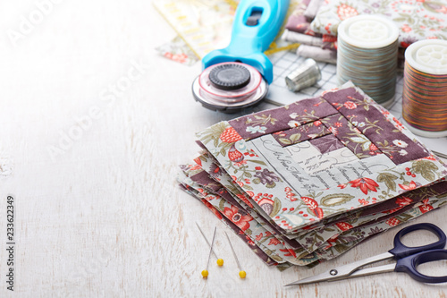 Patchwork log cabin blocks, stack of blocks, sewing accessories on white wooden surface