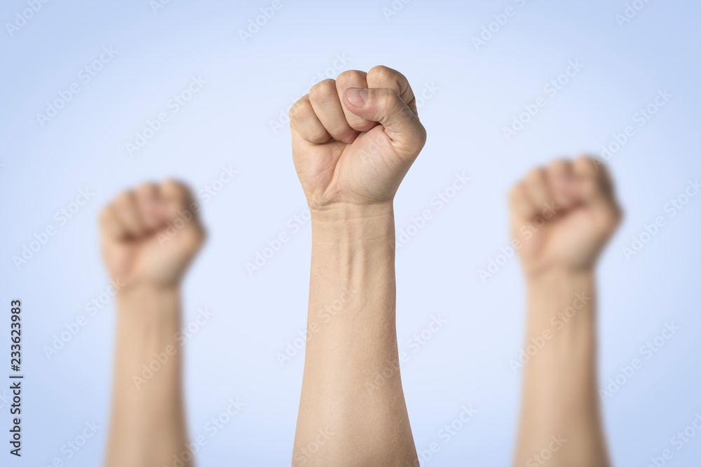 Male hands clenched into a fist and raised up on a blue background. Concept of power, rebellion, unity, revolution, riot Male hands clenched into a fist and raised up on a blue background. Concept of power, rebellion, unity, revolution, riot