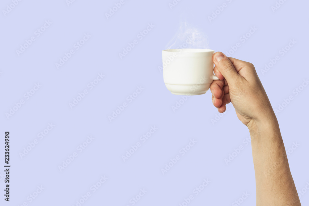Male hand holding a white cup with hot coffee or tea on a light blue background. Breakfast concept with hot coffee or tea Male hand holding a white cup with hot coffee or tea on a light blue background. Breakfast concept with hot coffee or tea