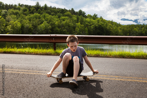 Φωτογραφία Boy looking at wounded knee while sitting on skateboard against railing