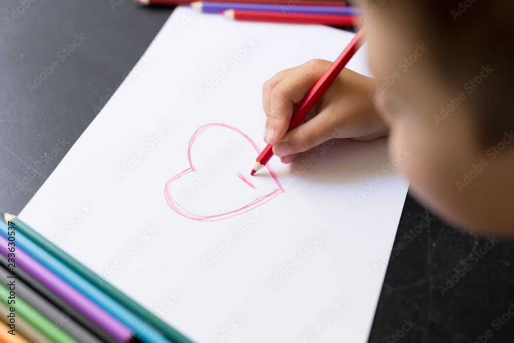 Kid's hand with pencil draws heart on white paper. Mother's day concept. Celebration. Hand made card. Kid's hand with pencil draws heart on white paper. Mother's day concept. Celebration. Hand made card.