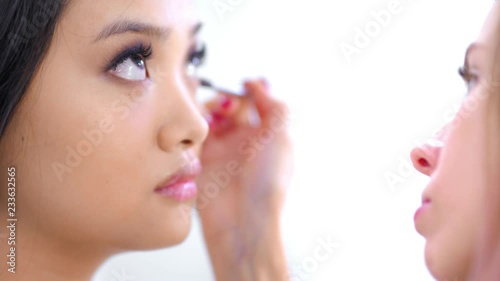 Attractive Asian young woman raising brown eyes up during working professional makeup artist closeup
